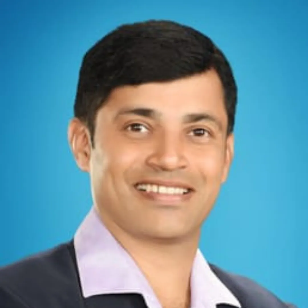 Headshot of Muralidhar K., Co-founder and CEO of Hardik Herbals, smiling and wearing a blazer over a light purple collared shirt, against a bright blue background. Client of OnlineShree.