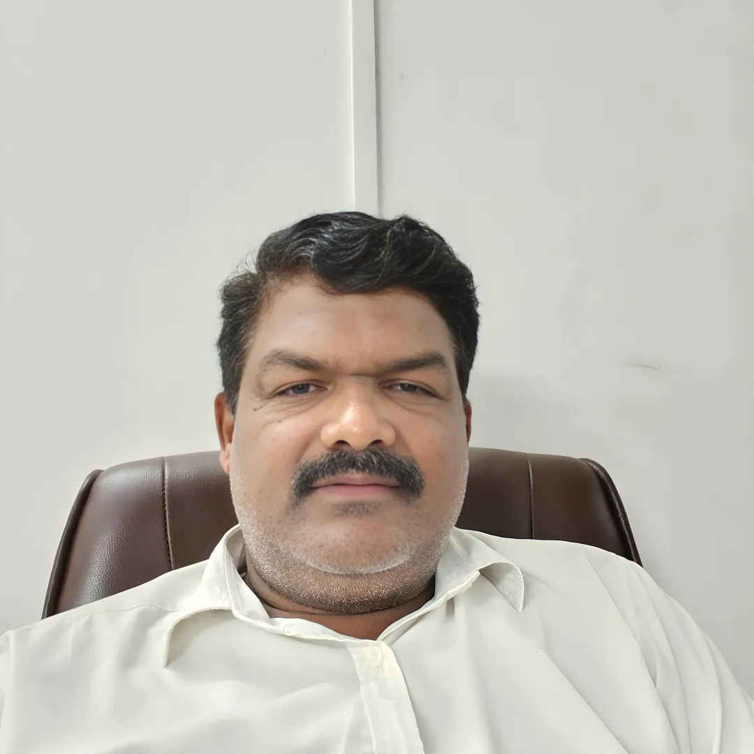 Headshot of Dr. B. Vinayachandra Shetty, an Ayurvedic Healthcare Professional and Founder of Kshemadhama, sitting in a leather chair and wearing a white collared shirt.