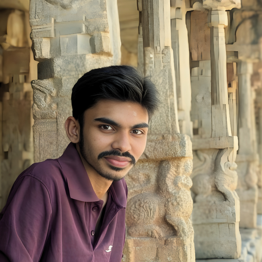 Photo of Pranava Bhat, a journalist and content creator, posing in a maroon polo shirt against the ornate stone pillars of an ancient temple or ruins.